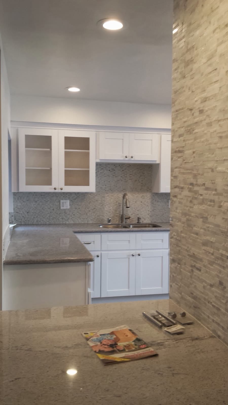 Completed addition interior — kitchen with white shaker cabinets, stone accent wall, and granite counters.