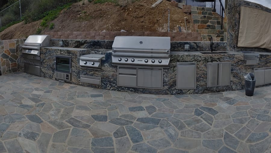 Outdoor kitchen with stainless grill, side burner, refrigeration, and stone counter.