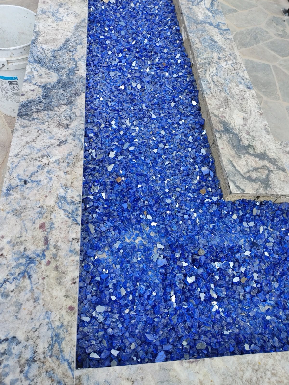 Custom outdoor fire pit filled with cobalt-blue fire glass, set between stone counter wings.