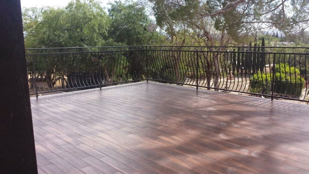 Finished wood-grain composite deck with wrought-iron railing and mature tree backdrop.