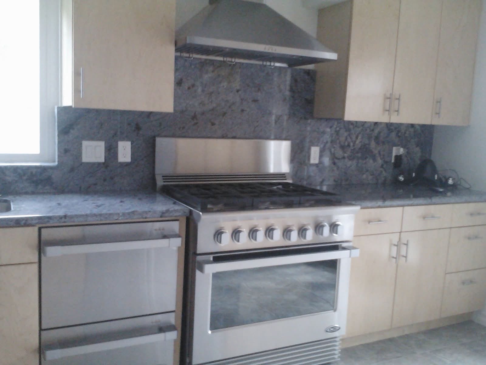 Kitchen build with light wood-grain cabinets, stainless gas range, vent hood, and granite counters.