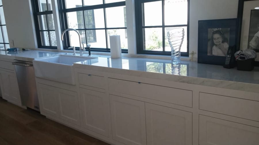 White shaker kitchen with farmhouse sink, marble counters, and steel-framed windows.