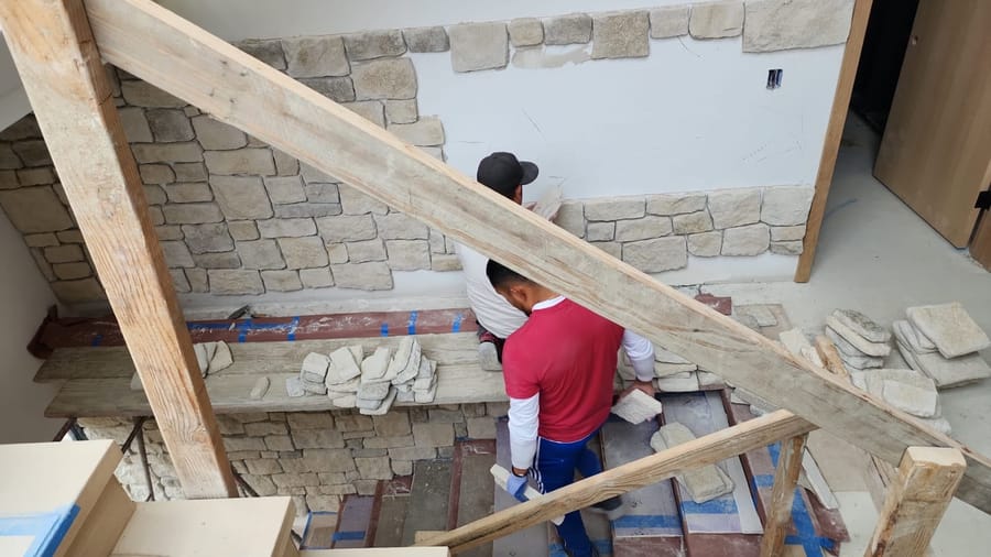 Exterior wall finish in progress on a VIP build — natural stone applied over a properly prepared envelope.