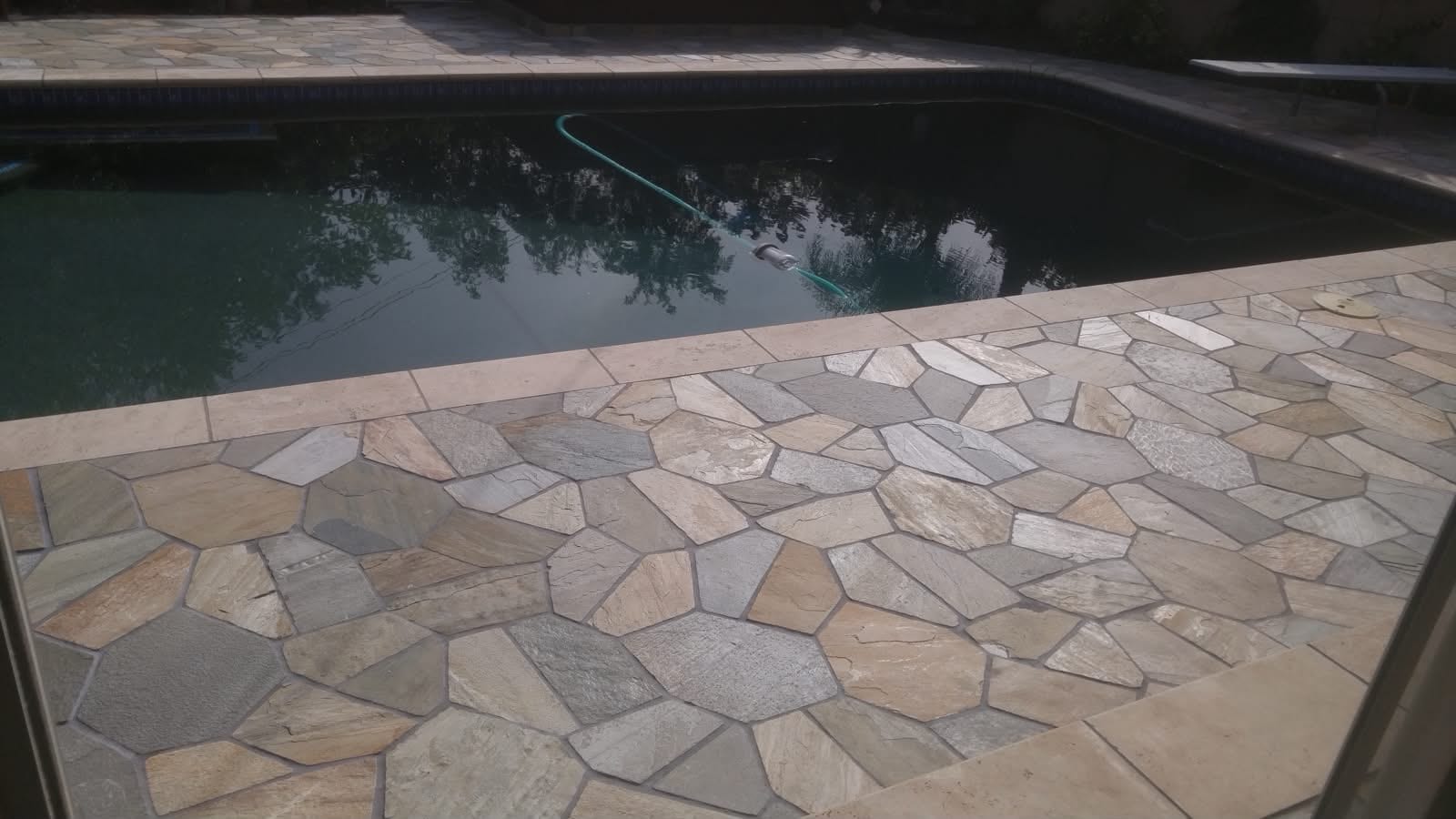 Custom in-ground pool with dark plaster interior, set into flagstone coping and patio.